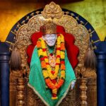 A serene and divine depiction of Sai Baba of Shirdi, seated in a meditative pose with a peaceful expression. He is wearing a simple white robe and headscarf, with a golden glow surrounding him, symbolizing his spiritual aura. The background features a sacred temple with soft golden light and incense smoke rising, creating a mystical atmosphere.