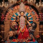 Devotees in traditional attire offering flowers to Goddess Durga during Pushpanjali ritual inside a decorated Durga Puja pandal in Kolkata.
